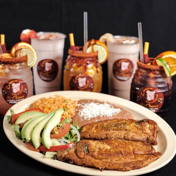 Mexican chiles rellenos with rice, beans, and salad, alongside various fruit drinks.
