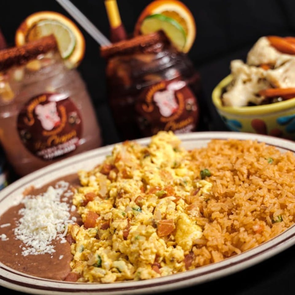 Mexican breakfast plate with scrambled eggs, refried beans, rice, and two micheladas.