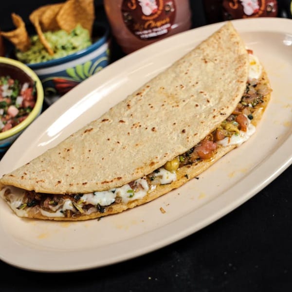A large quesadilla filled with melted cheese and vegetables, served with guacamole and salsa.