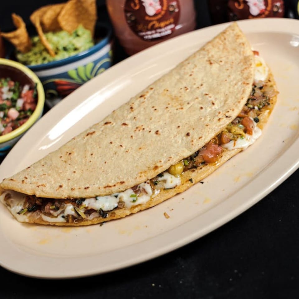A large quesadilla filled with melted cheese and vegetables, served with guacamole and salsa.