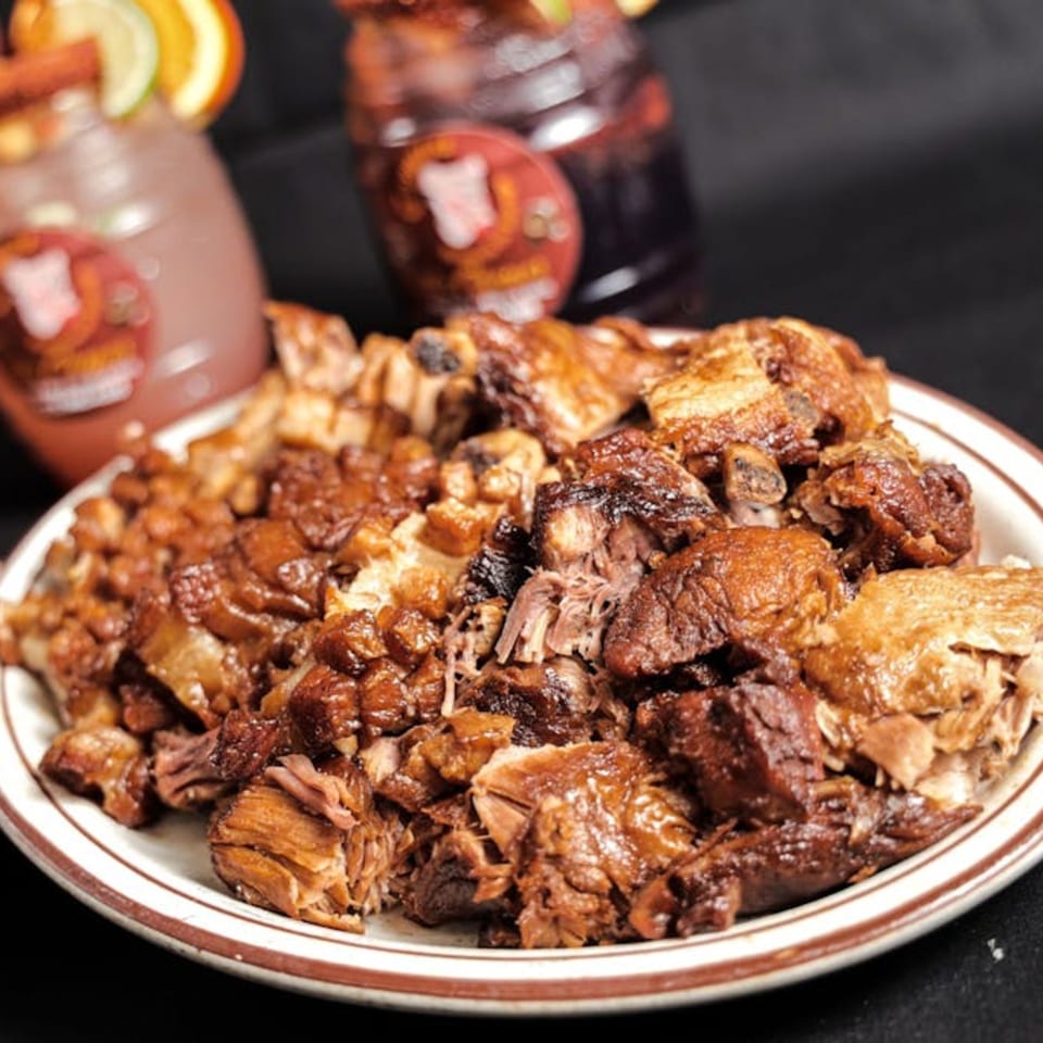 A plate of Los Chepes' Mexican carnitas, with two drinks garnished with fruit in the background.
