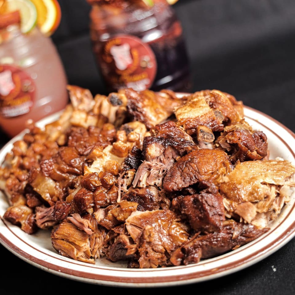 A plate of Los Chepes' Mexican carnitas, with two blurred drinks in the background.