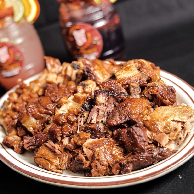 A plate of Los Chepes' Mexican carnitas, with two blurred drinks in the background.