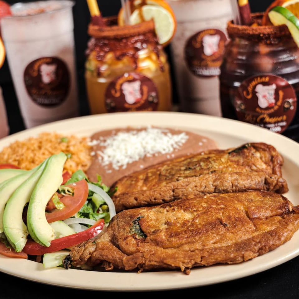 A plate of Mexican food with two chile rellenos, rice, refried beans, and a side salad.