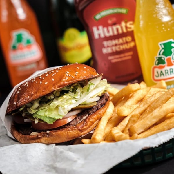 A Los Chepes burger with fries, ketchup, and two Jarritos sodas in the background.