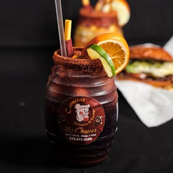A Los Chepes Mexican drink in a barrel-shaped glass, garnished with orange, lime, and chili candy.