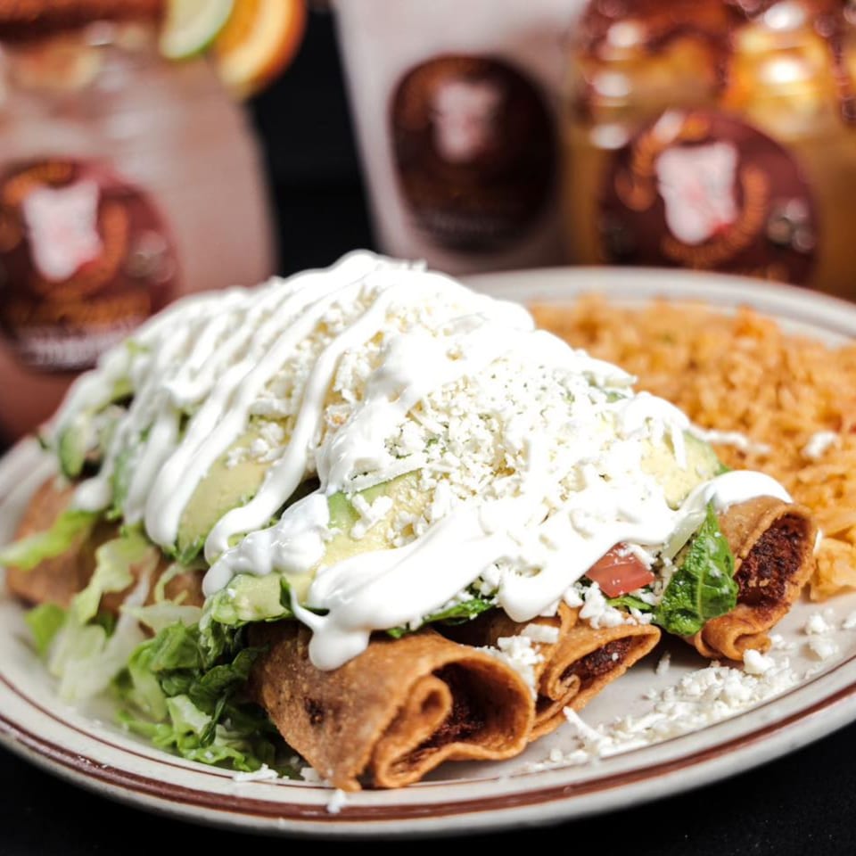 Mexican taquitos topped with sour cream, avocado, lettuce, and cheese, served with rice.